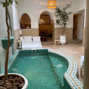 Área de piscina com espreguiçadeira, planta em vaso e um banquinho.