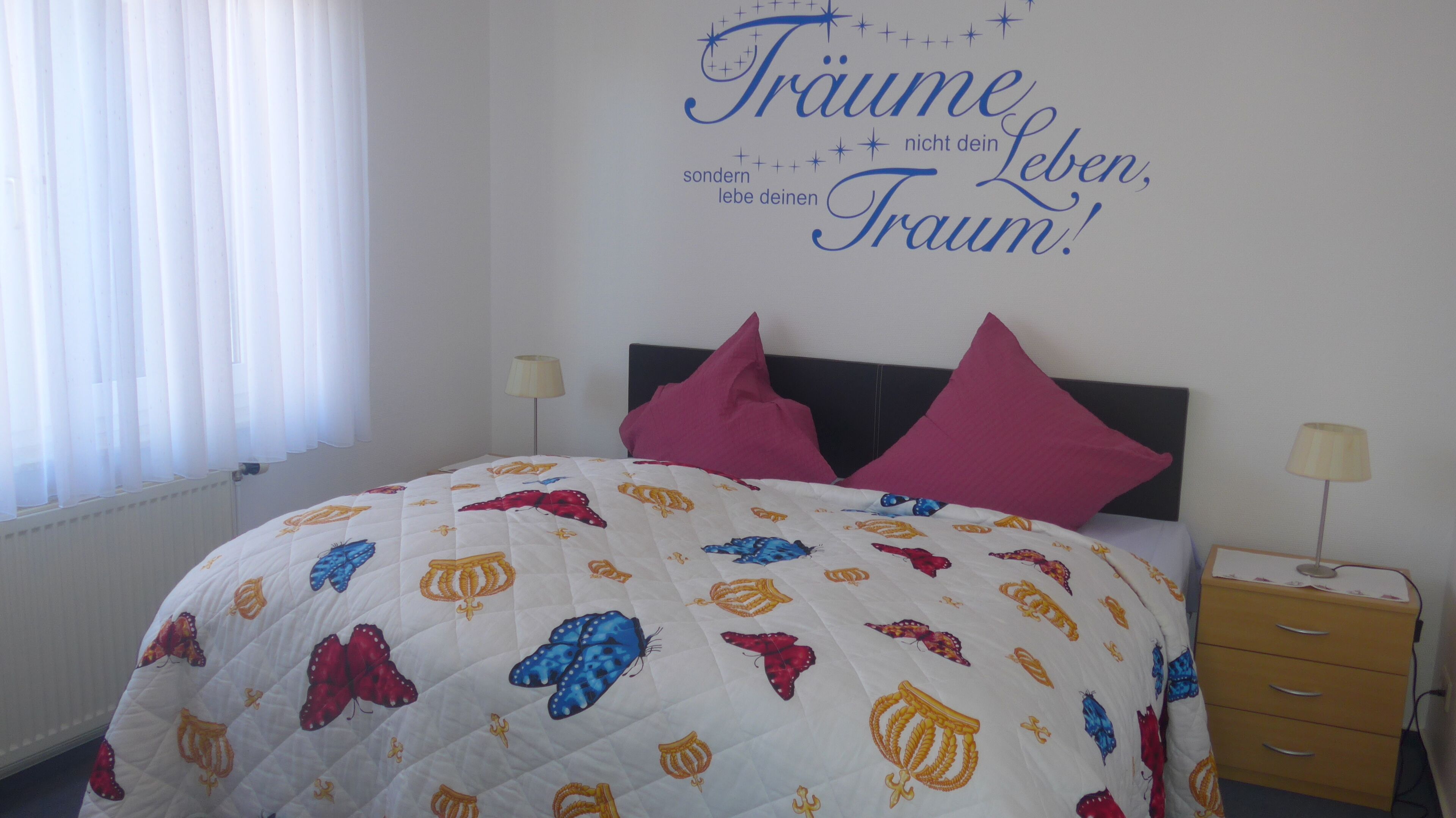 Un dormitorio con cama, dos almohadas, una mesita de noche y un adorno en la pared.
