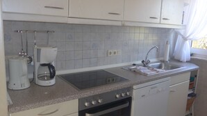 A kitchen with white cabinets, a built-in oven, a dishwasher, a coffee maker, and a sink. - Haus Eveline (Borkum)