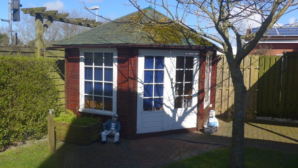 A small, single-story building with a red brick exterior and white trim. It features a large window with multiple panes and a white door. - Haus Eveline (Borkum)