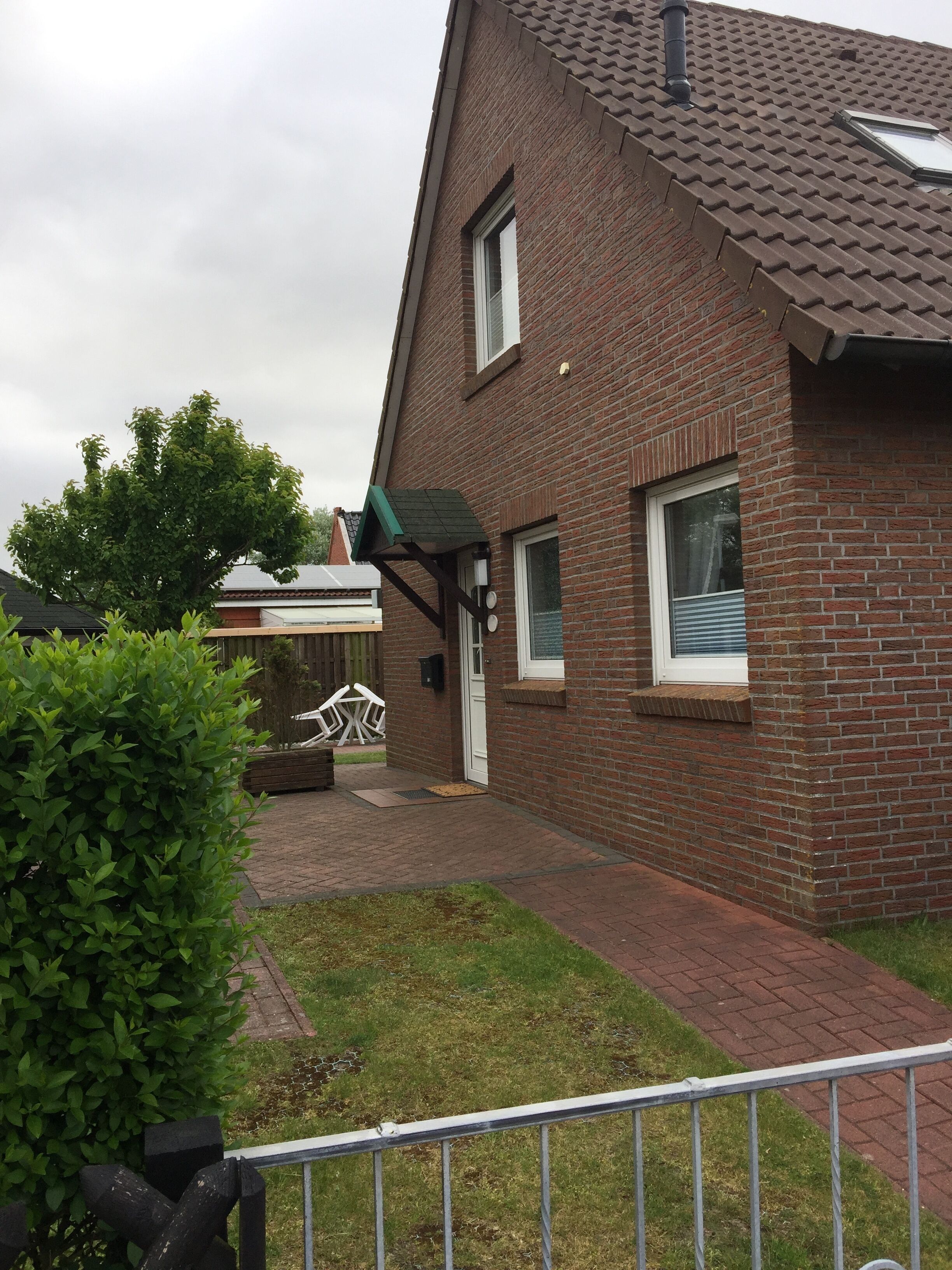 A brick house with a sloped roof, a visible chimney, and a small front yard with a metal fence.
