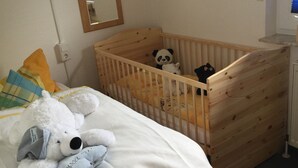 A bedroom with a wooden crib, a bed with a white comforter, and a stuffed panda bear on the bed. - Haus Eveline (Borkum)