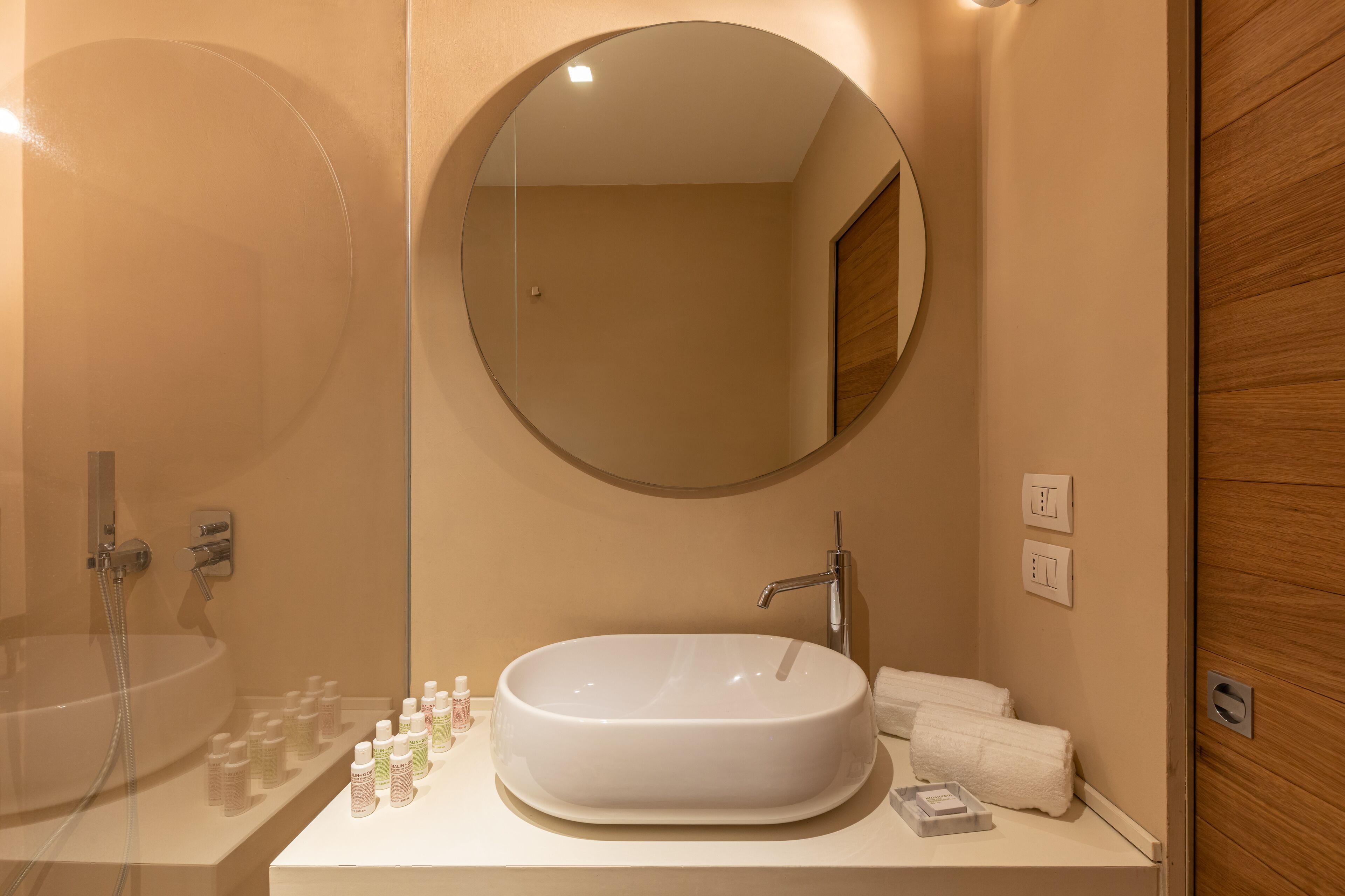 Ein modernes Badezimmer mit einem großen, ovalen Waschbecken, einem runden Spiegel und einer Holztür.
