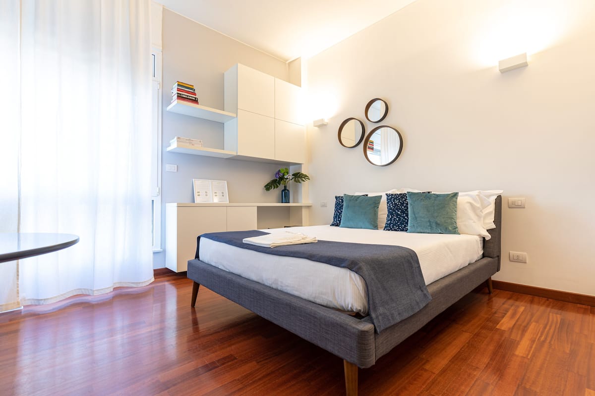 A modern bedroom with a bed, bedside tables, a desk, and built-in shelving.