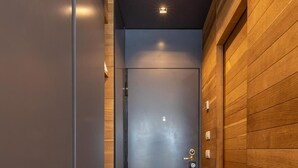 Un pasillo con una puerta oscura, paneles de madera a un lado y suelo de baldosas.