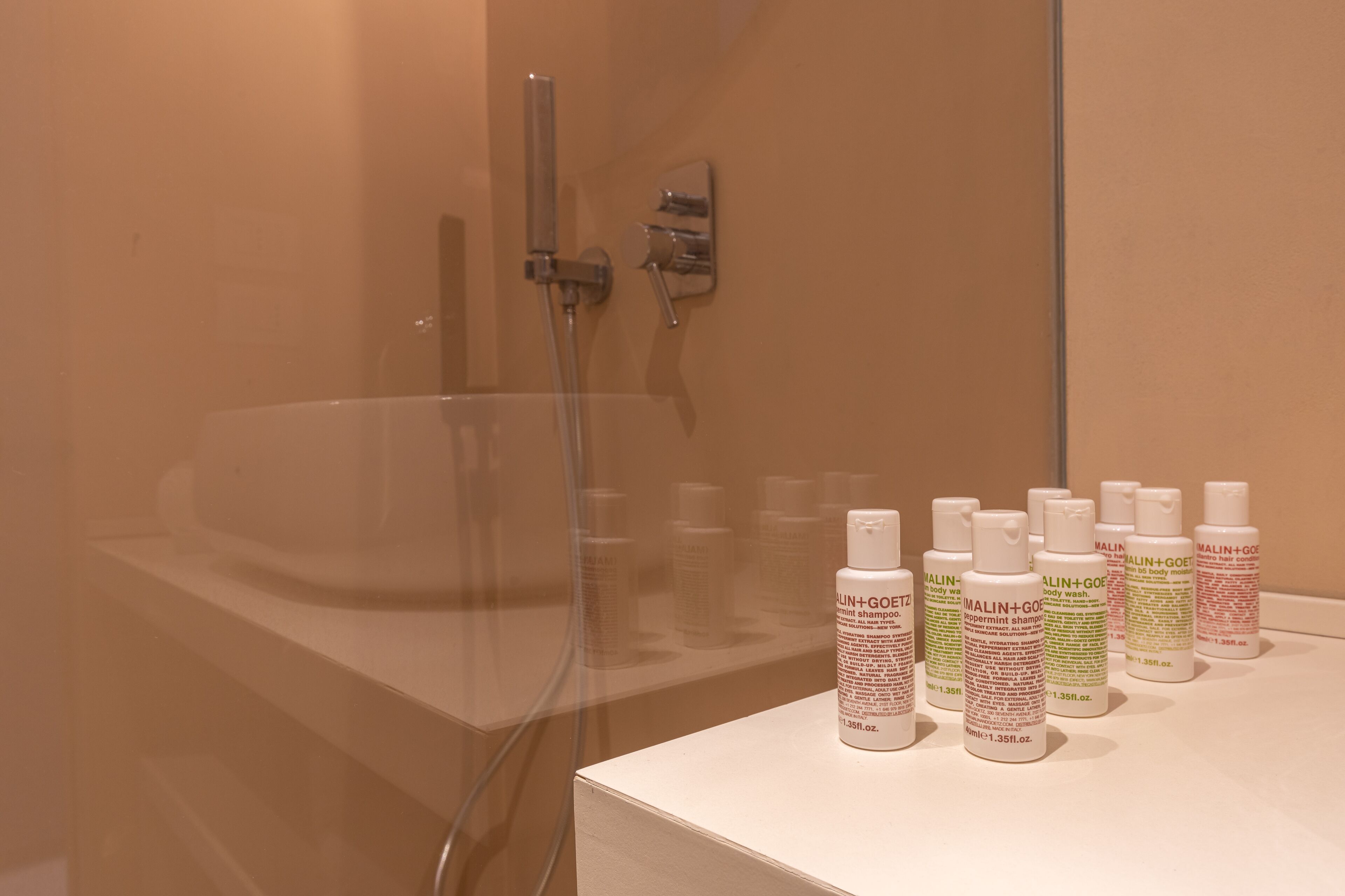 Une salle de bain avec une grande baignoire, une douche en verre et plusieurs flacons de gel douche posés sur un comptoir.