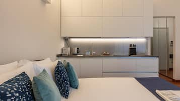Een moderne hotelkamer met een bed, een kleine kitchenette en een badkamer zichtbaar door een glazen deur.