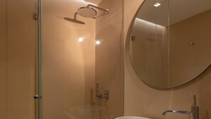 Un baño moderno con ducha envuelta en vidrio, un espejo redondo grande, un lavabo blanco y un perchero para toallas.