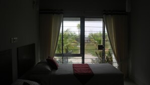 Een hotelkamer met een bed, gordijnen en uitzicht op palmbomen en een gebouw.