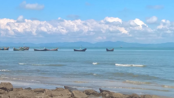 A beach with several boats anchored in calm waters, a clear sky, and distant mountains.