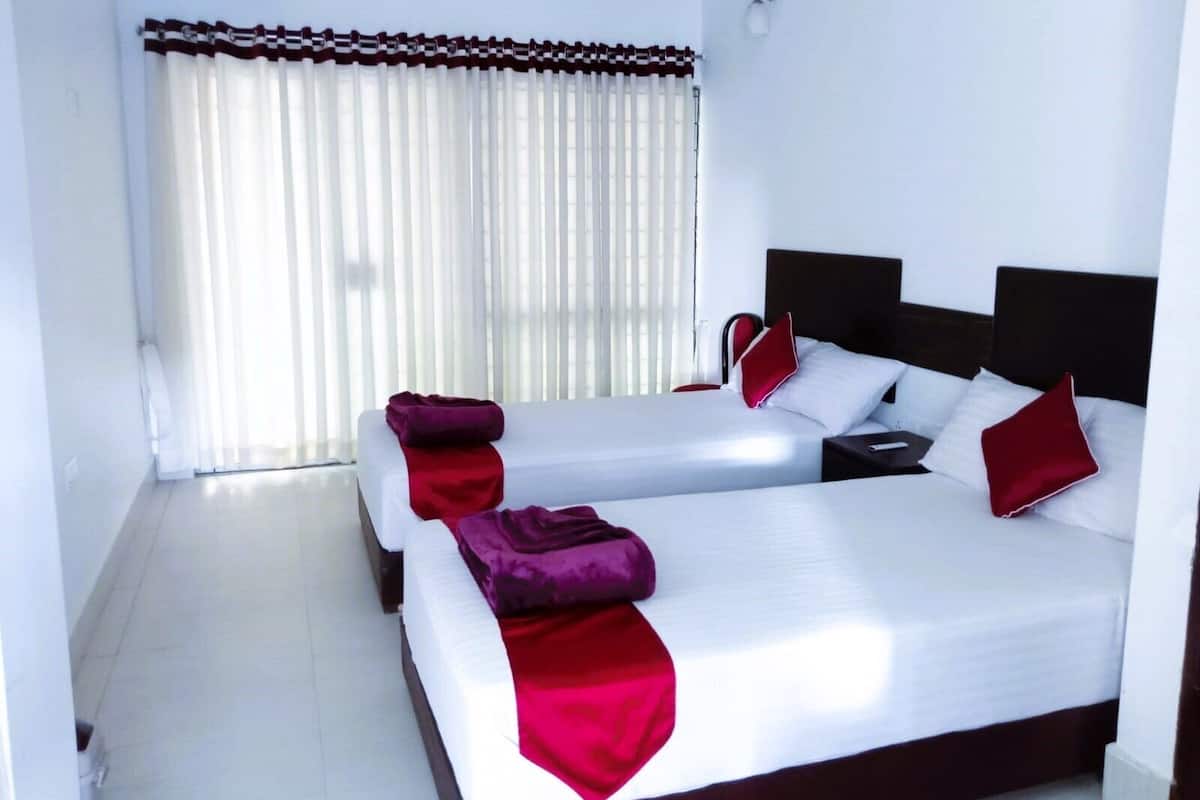 A hotel room with two beds, white bedding, red pillows, and a large window with sheer curtains.
