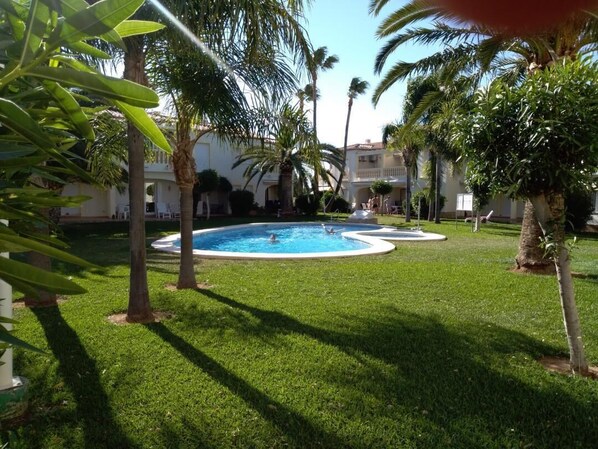 A pool area with palm trees and a building in the background. - Attractive bungalow in a quiet residential complex with pool (Dénia)