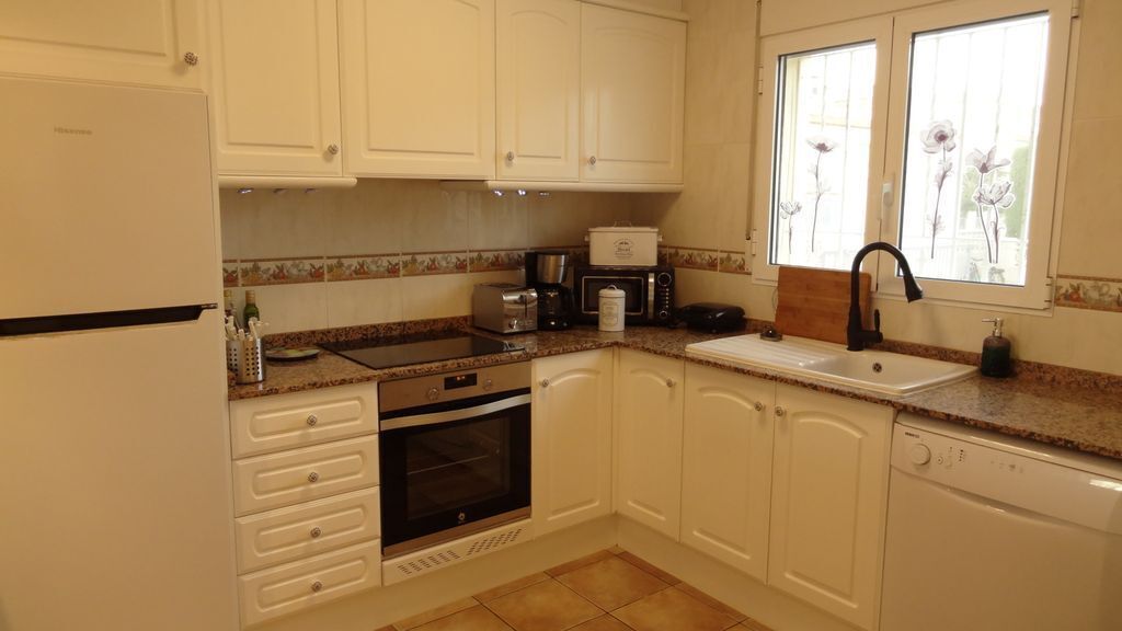 A kitchen with white cabinets, a stove, oven, microwave, toaster, and a sink with a faucet.