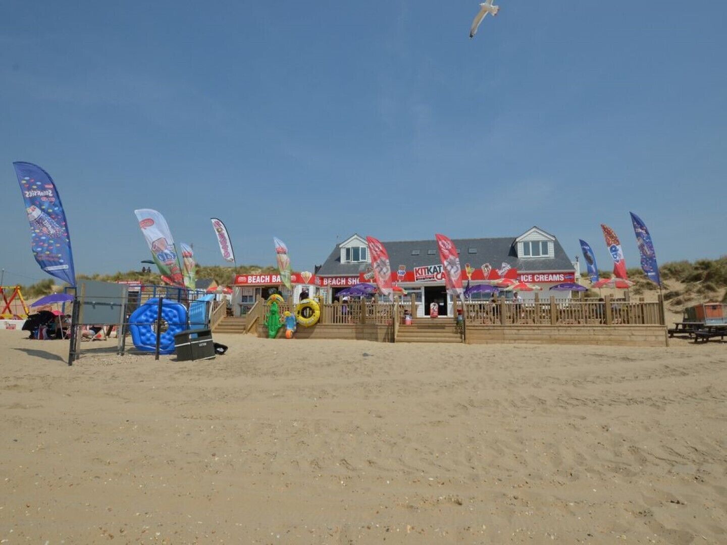 Un edificio frente a la playa con varias banderas, una torre de salvavidas y equipo de playa.