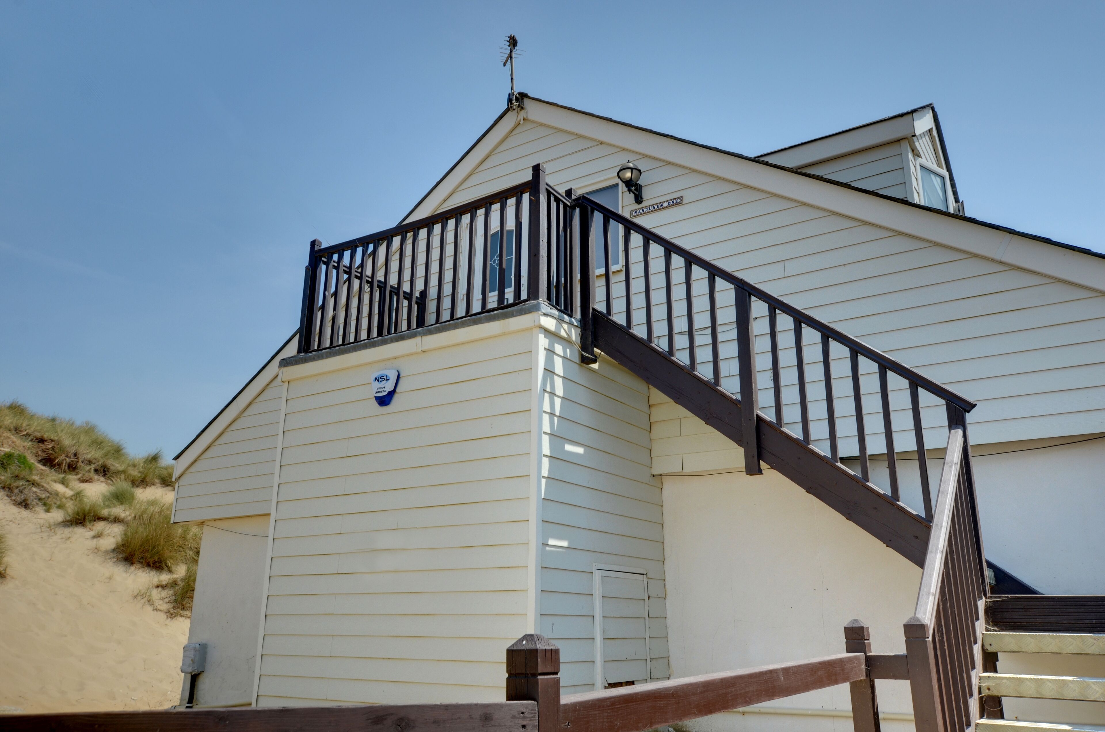 A beach house with a balcony and a staircase leading to the upper floor.