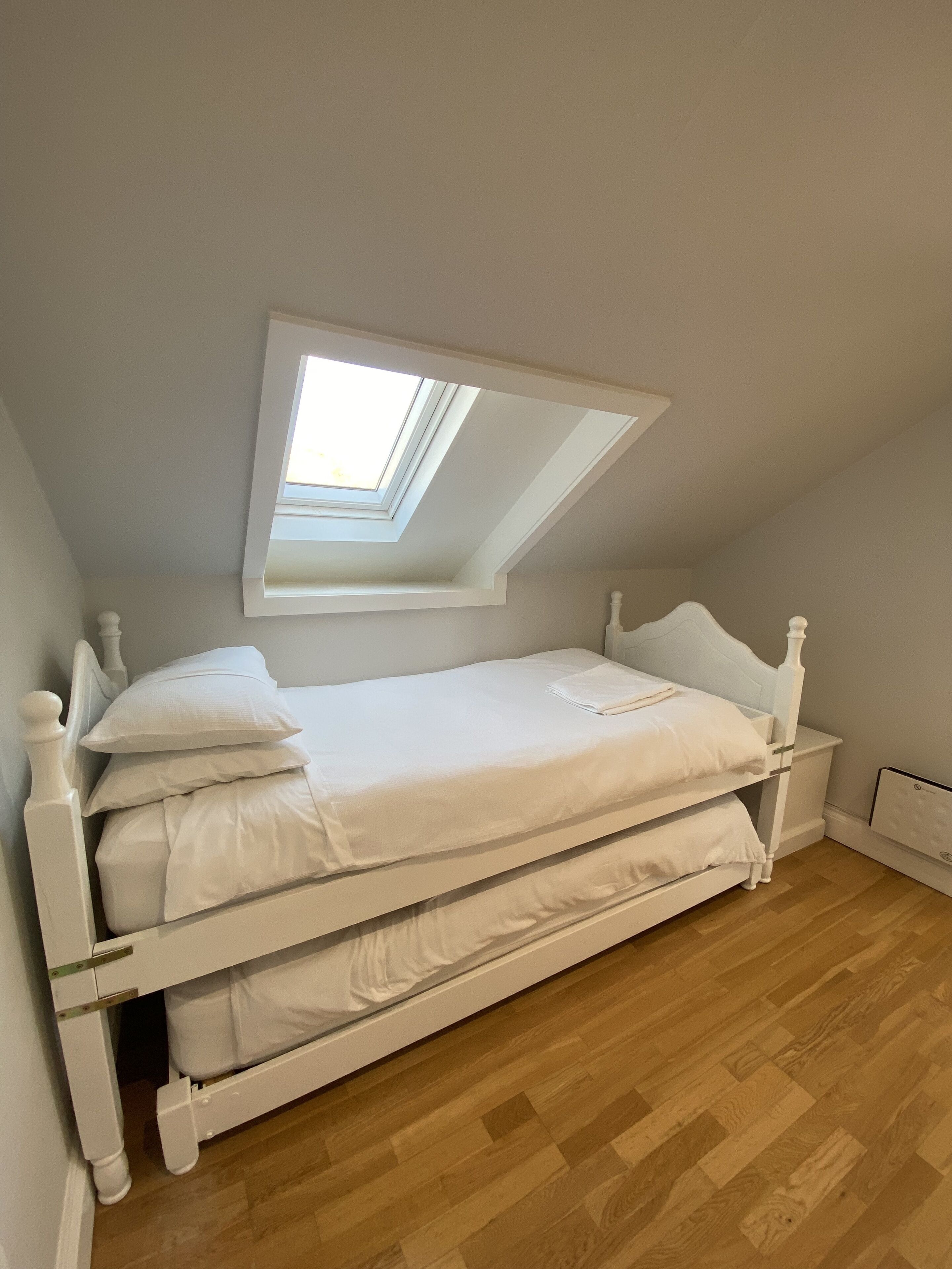 A white bed in a room with a sloped ceiling and a skylight.