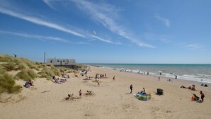 A beach with people sunbathing and swimming, a lifeguard tower, and a clear sky. -  Sandunes 2    (Camber)