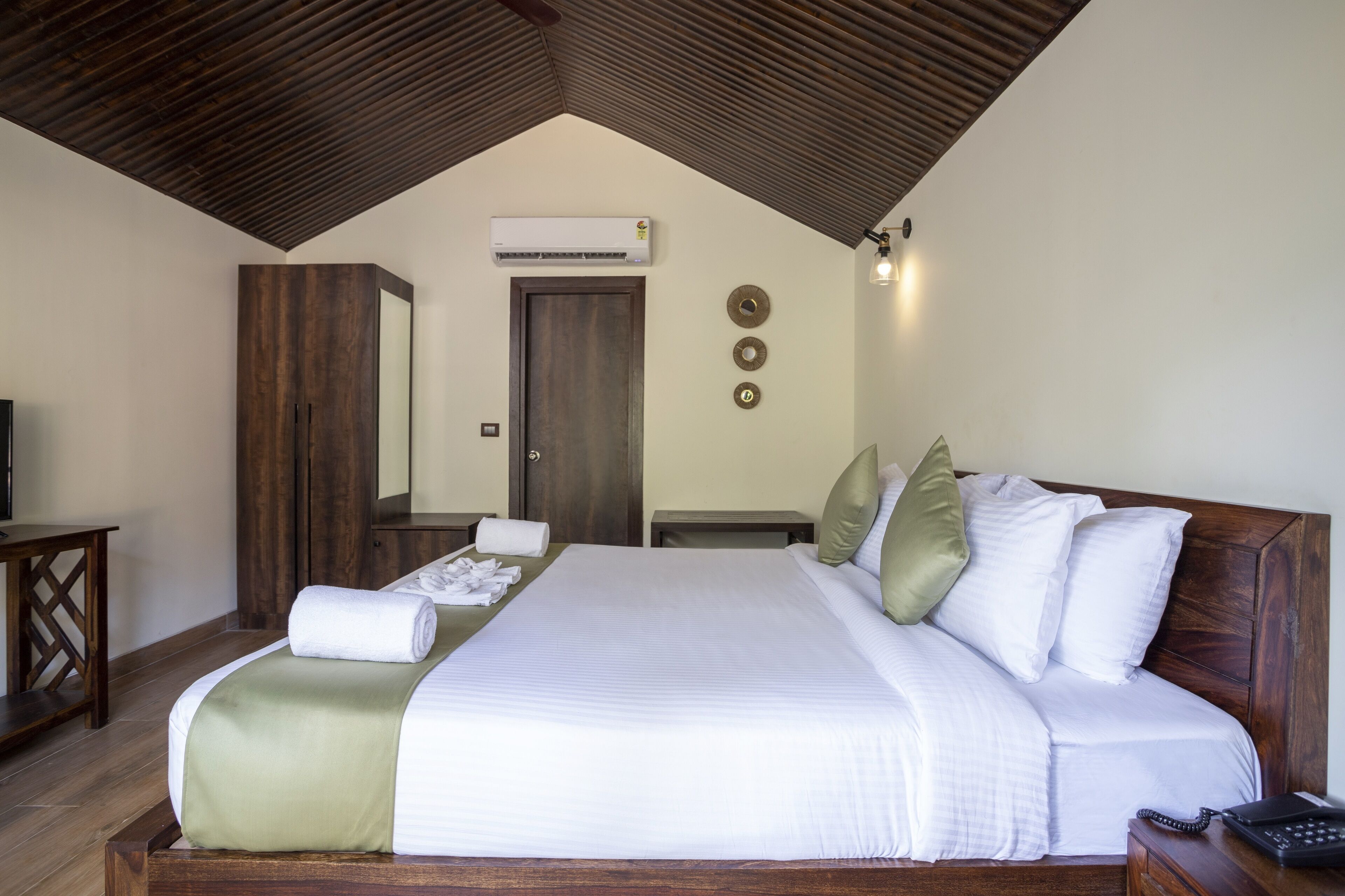 A neatly made bed with pillows, a bedside table, a wooden wardrobe, and an air conditioning unit on the wall.