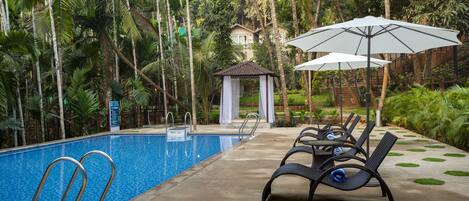 A pool area with lounge chairs and umbrellas, surrounded by lush greenery and a gazebo.