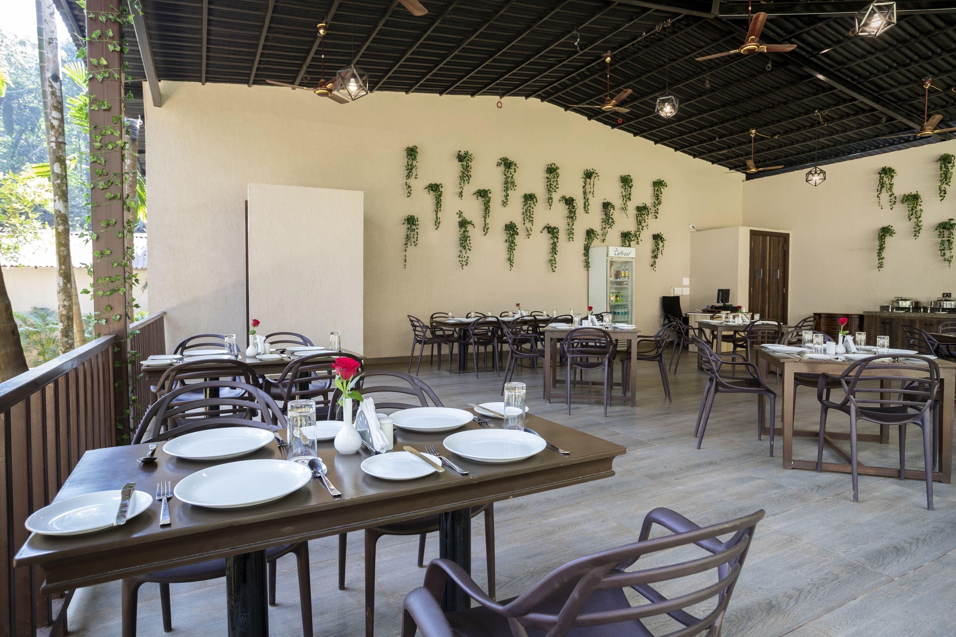 A restaurant with multiple tables set for dining, a ceiling fan, and hanging plants.