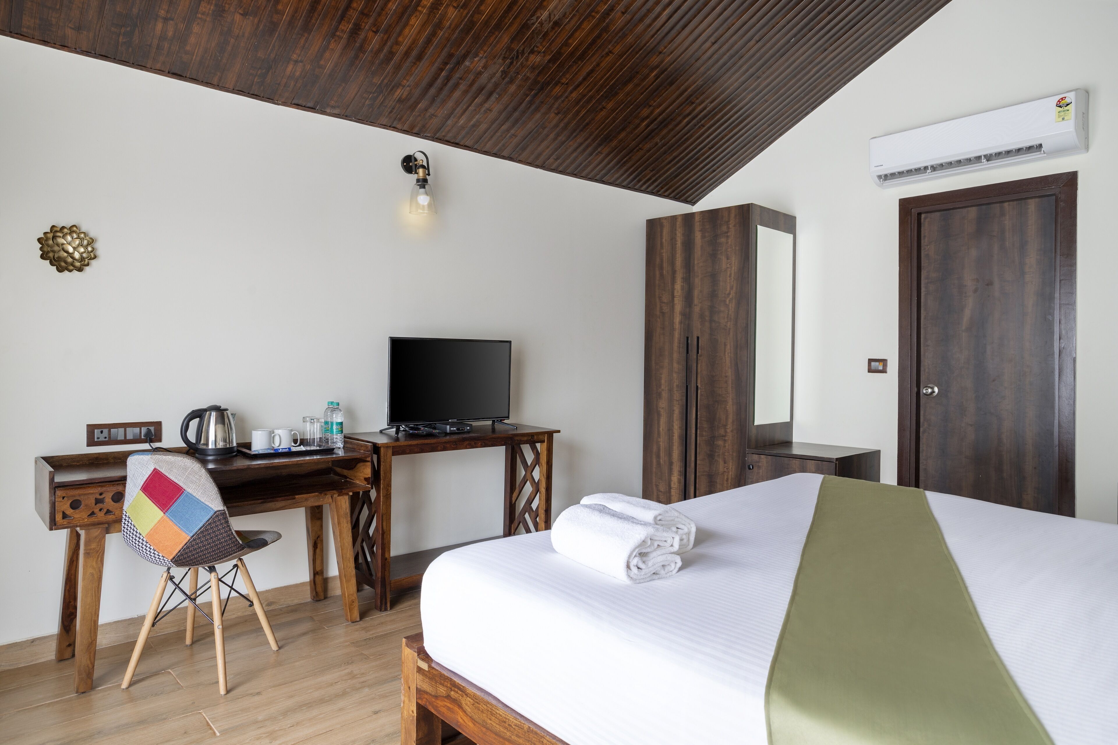 A hotel room with a bed, a desk with a television, a chair, and a wardrobe.