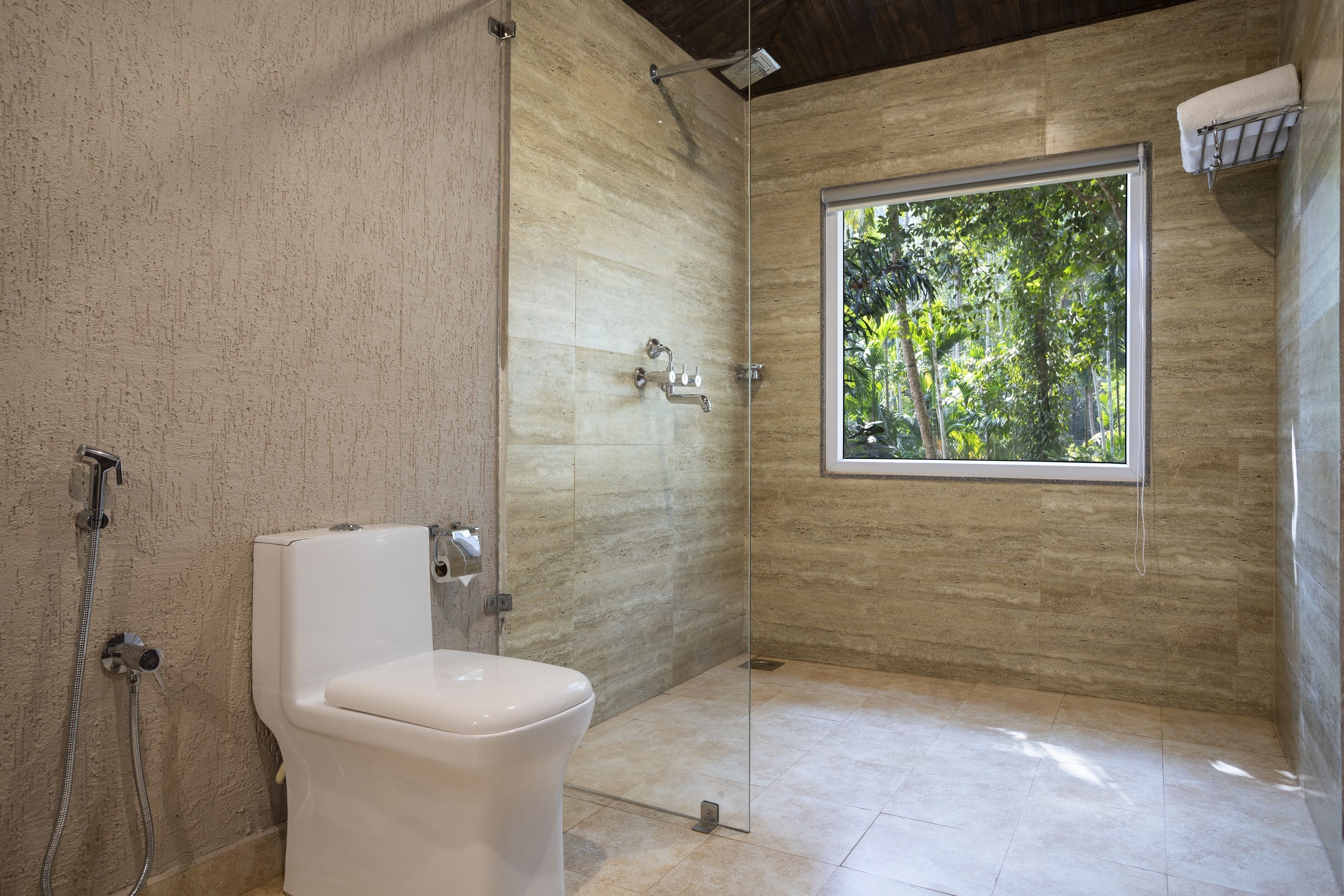 A modern bathroom with a glass shower enclosure, a toilet, and a window providing a view of greenery.
