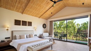 Ein geräumiges Schlafzimmer mit einem großen Bett, einer Sitzecke und einem Balkon mit Blick auf Bäume.