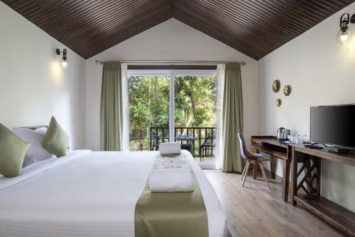 A bedroom with a bed, a desk, a television, and a balcony with curtains.
