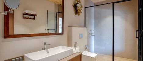 A modern bathroom with a large mirror, a wooden vanity, a white sink, and a glass shower enclosure.