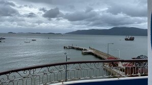A coastal view with a pier extending into calm waters, surrounded by boats and distant mountains. - Hotel Zibamba (São Francisco do Sul)