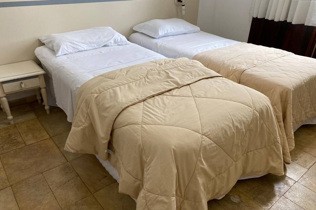 Hotellihuone, jossa on kaksi erillistä sänkyä, yöpöytä ja laatoitettu lattia.
