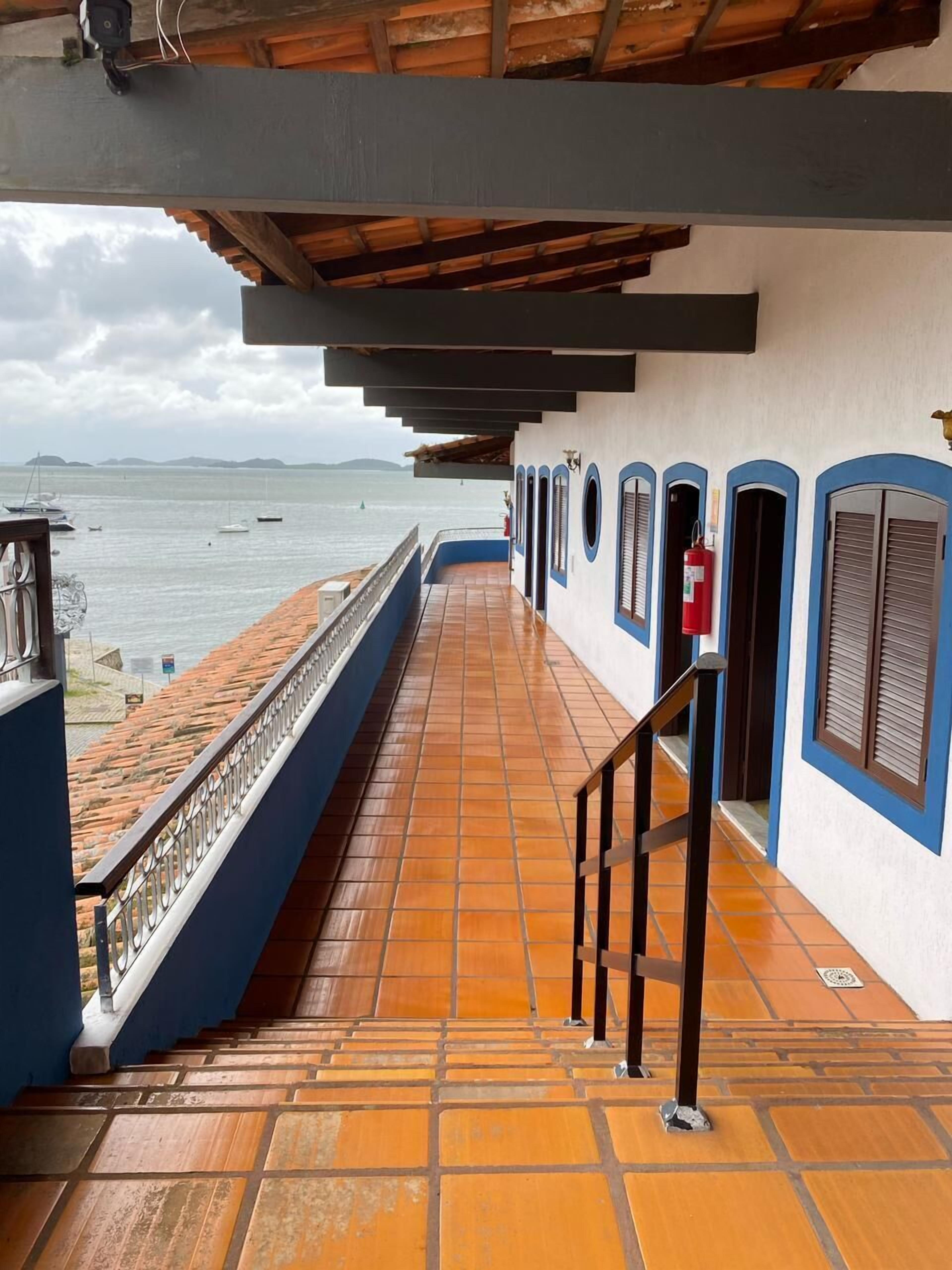 A covered outdoor area with a tiled floor, a metal railing, and a view of the sea.