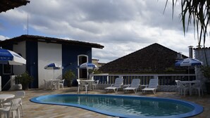A swimming pool area with lounge chairs and umbrellas, surrounded by tiled flooring and a building with a tiled roof. - Hotel Zibamba (São Francisco do Sul)