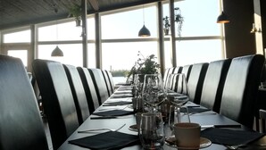 A restaurant with a long table set for dining, large windows, and a wooden ceiling. - Nordic Lapland Resort (Kalix)