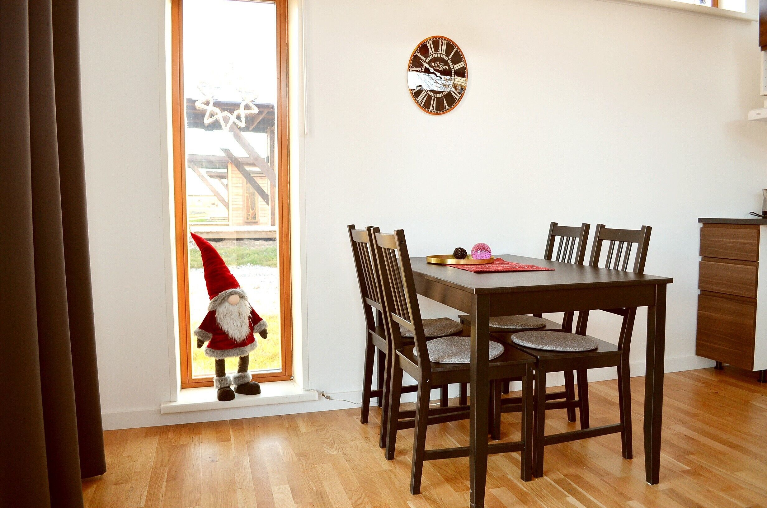 Un coin repas avec une table et des chaises en bois, une horloge au mur et une fenêtre avec des rideaux.