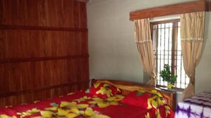 A room with a wooden ceiling, a bed with a floral bedspread, a window with curtains, and a plant on the windowsill.