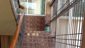 Escadaria com corrimão de madeira e guarda-corpo de metal, que leva a um patamar com vista para a vegetação lá fora.