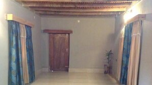 Um corredor com uma porta de madeira no final, emoldurado por cortinas, e um vaso de planta à direita.