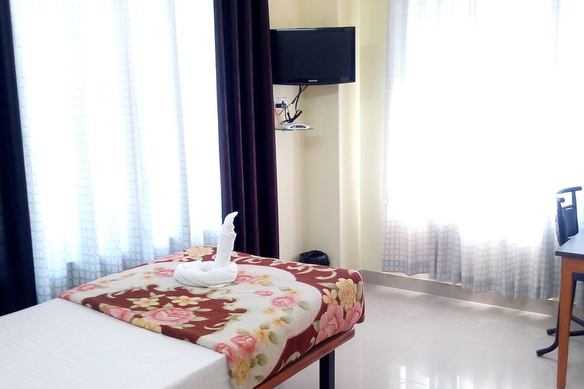 Una habitación de hotel con una cama, un televisor de pantalla plana en la pared y un escritorio con una silla.