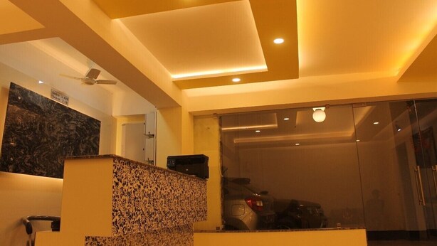 A reception area with a marble counter, ceiling lights, and a visible car through a glass door. - Hotel Niladrii Galaxy (Siliguri)