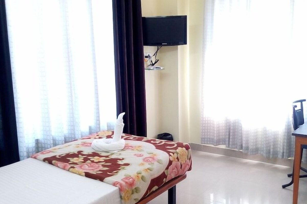 A hotel room with a bed, a flat-screen TV mounted on the wall, and a desk with a chair.