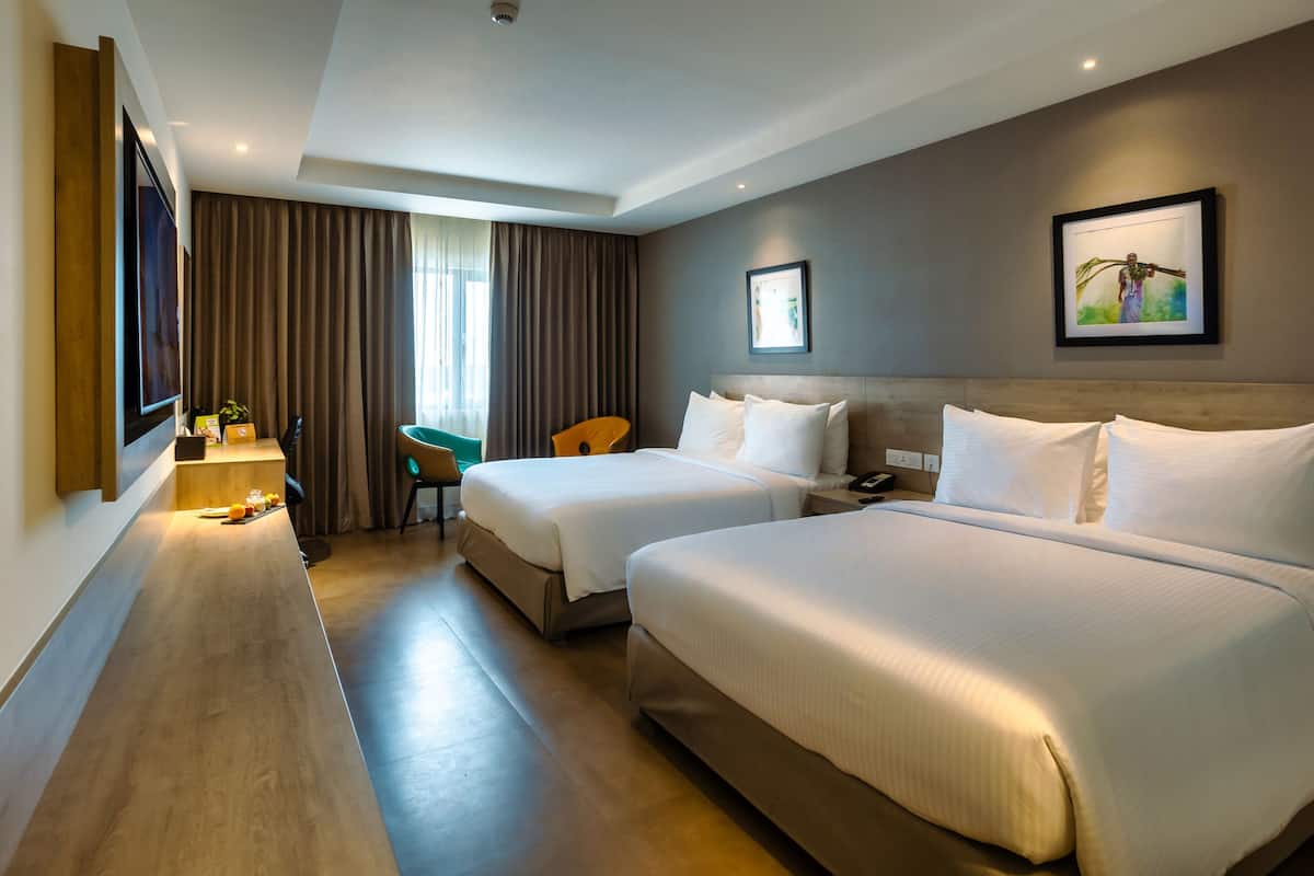 Une chambre d’hôtel avec deux lits, un bureau avec une chaise, un téléviseur à écran plat et une grande fenêtre avec des rideaux.