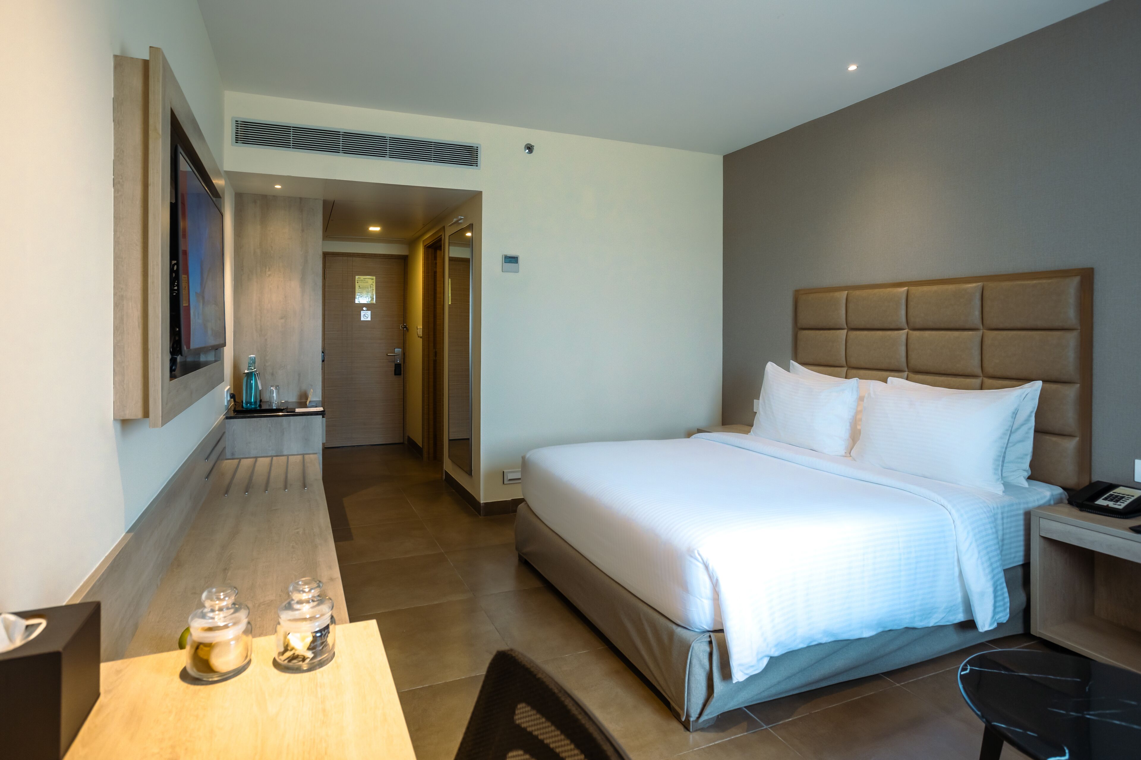 Habitación de hotel con una cama grande, una mesita de noche con teléfono, un escritorio con silla y una pequeña mesa con dos frascos.