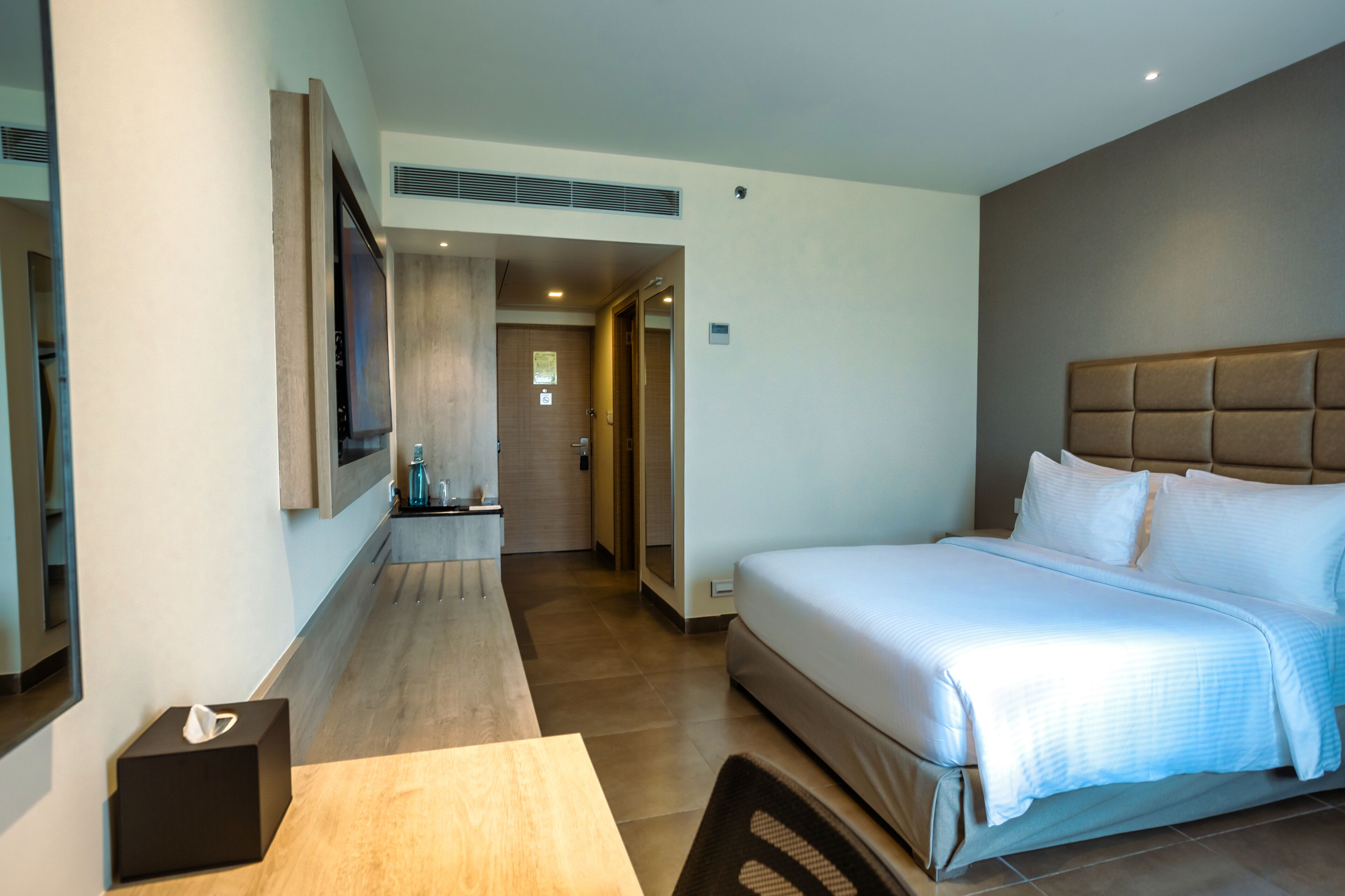 Una habitación de hotel moderna con una cama grande, un televisor de pantalla plana montado en la pared, una mesita de noche con caja de pañuelos y suelo de madera.