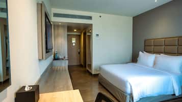 Una habitación de hotel moderna con una cama grande, un televisor de pantalla plana montado en la pared, una mesita de noche con caja de pañuelos y suelo de madera.
