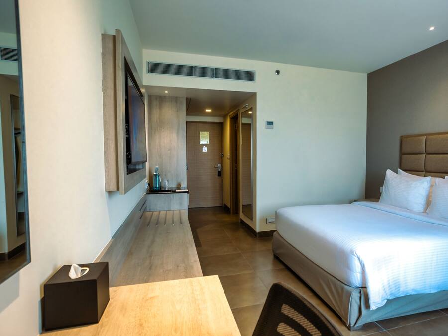 Una habitación de hotel moderna con una cama grande, un televisor de pantalla plana montado en la pared, una mesita de noche con caja de pañuelos y suelo de madera.