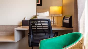 Habitación de hotel con escritorio, silla, espejo, lámpara y ventana con cortinas.