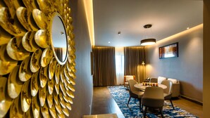 Una habitación de hotel moderna con comedor, un espejo grande y una alfombra azul estampada.