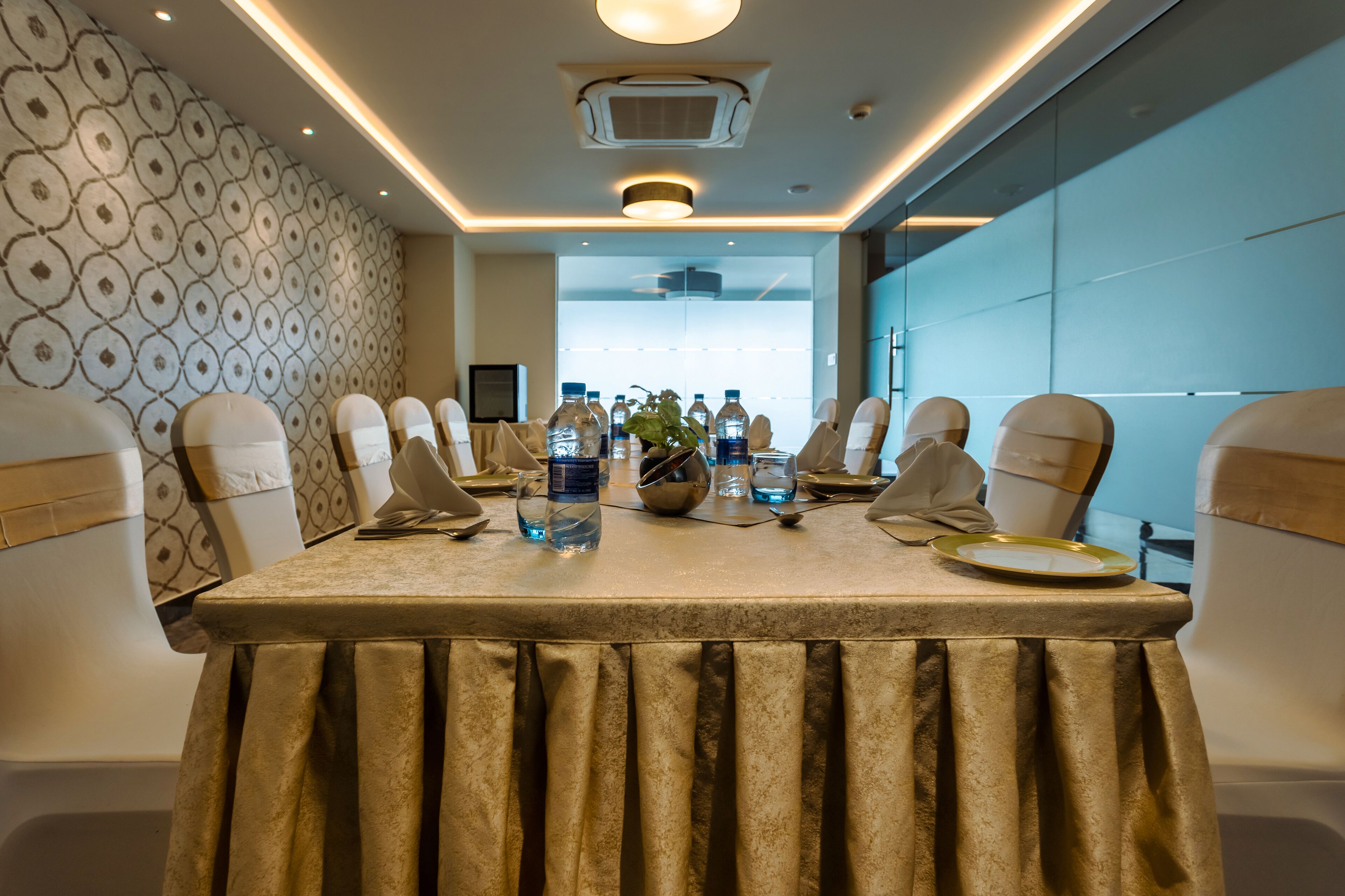 A conference room with a long table, chairs, water bottles, and a plant.