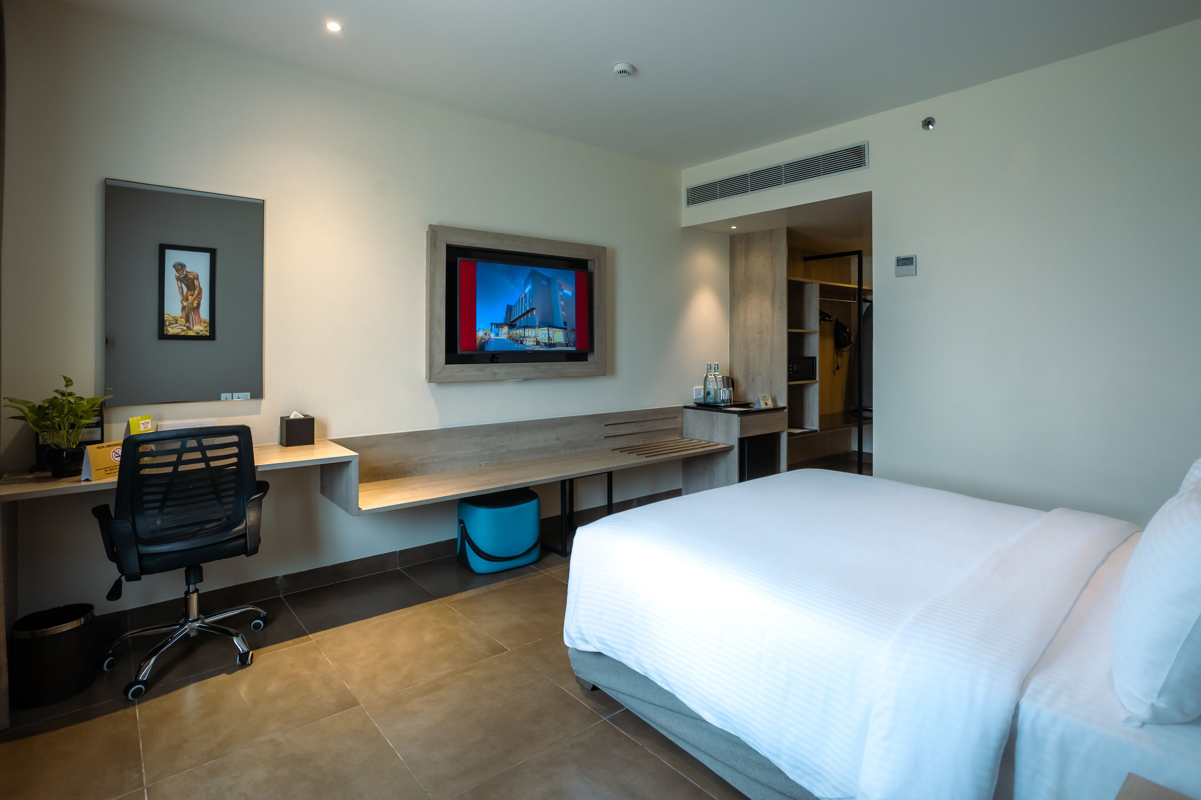 A modern hotel room with a bed, a desk with a chair, a television, and a wardrobe.